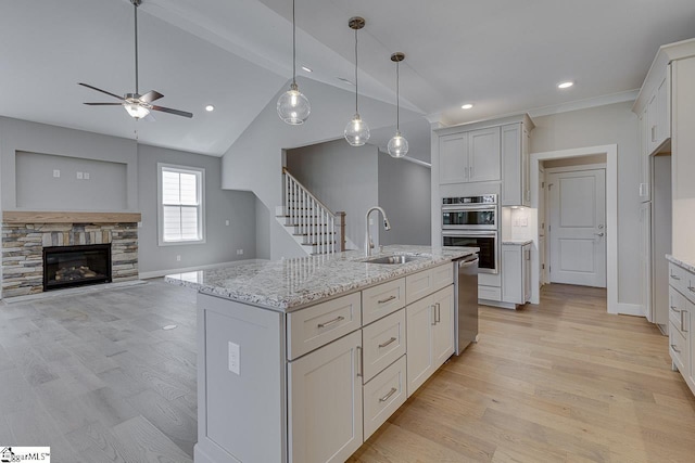 kitchen featuring light wood-style flooring, stainless steel double oven, light stone countertops, ceiling fan, and a sink