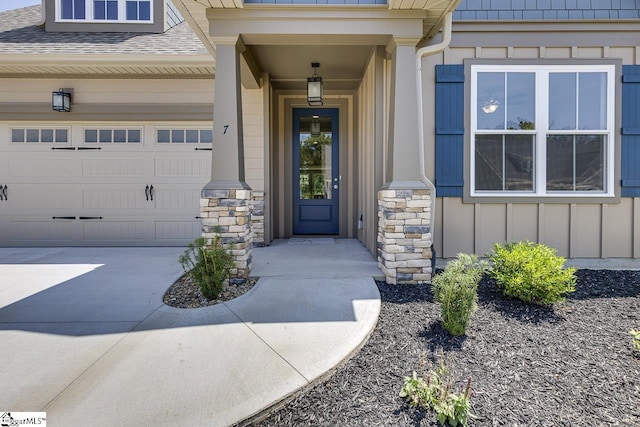view of exterior entry with roof with shingles, board and batten siding, a garage, and driveway