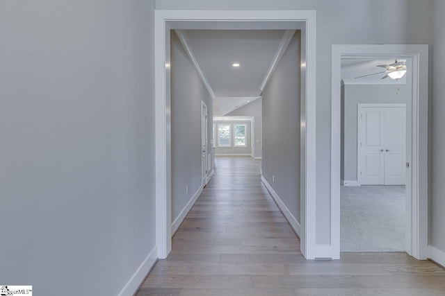 hall with ornamental molding, baseboards, and light wood-type flooring