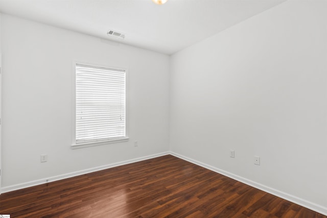spare room with dark wood-style flooring, visible vents, and baseboards