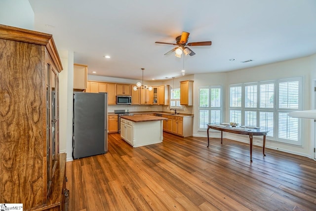 kitchen with dark wood-style flooring, a kitchen island, appliances with stainless steel finishes, ceiling fan with notable chandelier, and a sink
