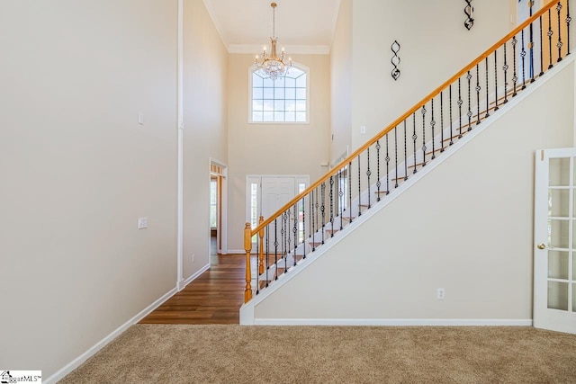 foyer featuring a notable chandelier, baseboards, stairway, carpet flooring, and a high ceiling