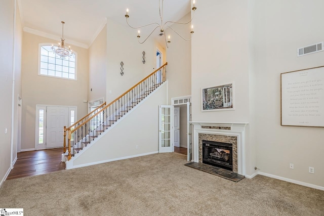 unfurnished living room with ornamental molding, a chandelier, carpet flooring, stairs, and visible vents