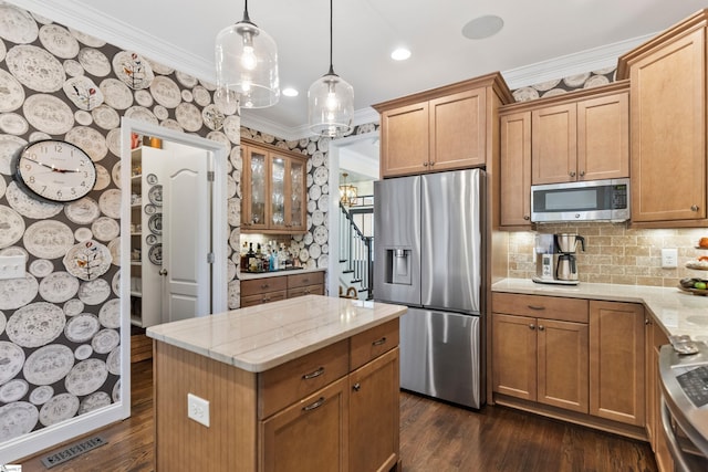 kitchen with appliances with stainless steel finishes, dark wood-style flooring, ornamental molding, and light stone countertops