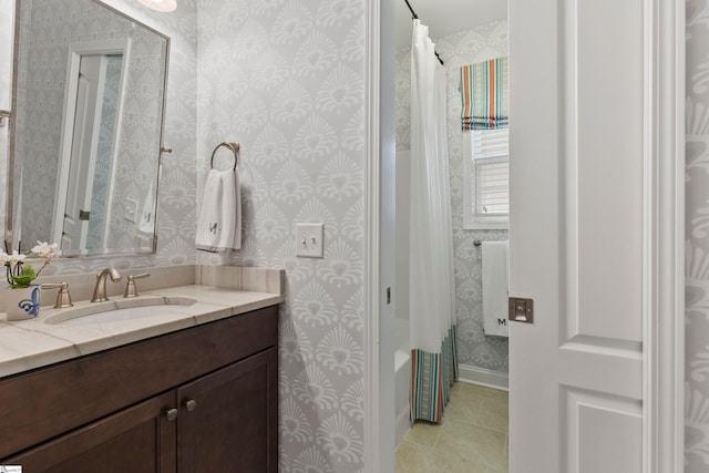 full bath featuring vanity, tile patterned floors, wallpapered walls, shower / bath combo with shower curtain, and baseboards