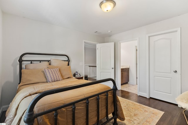 bedroom with ensuite bathroom, baseboards, and dark wood finished floors