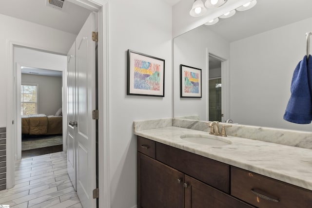 ensuite bathroom with visible vents, connected bathroom, vanity, wood finished floors, and a shower with door