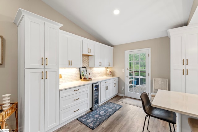 kitchen with tasteful backsplash, light wood-type flooring, white cabinets, vaulted ceiling, and wine cooler