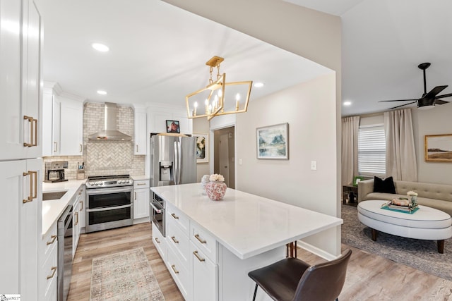 kitchen with light wood-style flooring, wall chimney exhaust hood, decorative backsplash, and appliances with stainless steel finishes