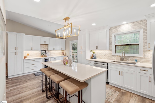 kitchen with stainless steel dishwasher, a sink, vaulted ceiling, and a wealth of natural light