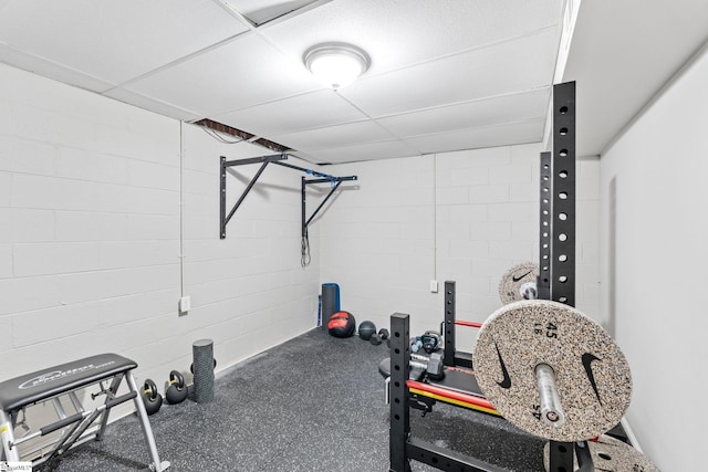 exercise room with a drop ceiling and concrete block wall