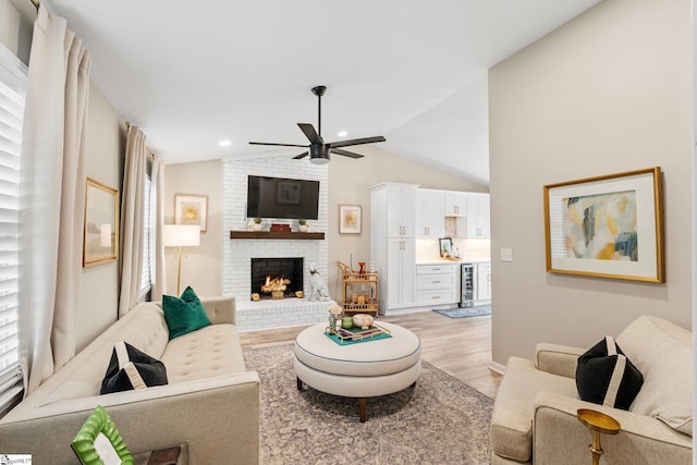 living room featuring ceiling fan, light wood-style flooring, vaulted ceiling, a brick fireplace, and wine cooler