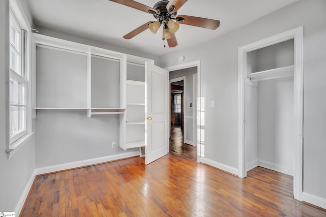 unfurnished bedroom with wood-type flooring, baseboards, multiple windows, and ceiling fan