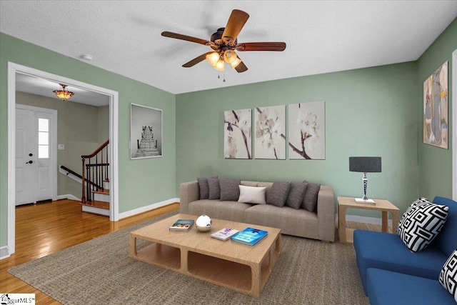 living area featuring stairs, ceiling fan, baseboards, and wood finished floors