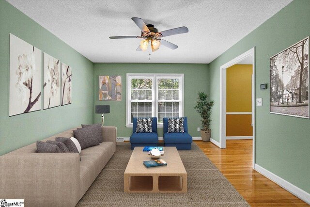 living room featuring a textured ceiling, wood finished floors, baseboards, and a ceiling fan