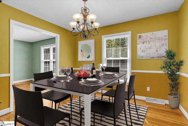 dining area with visible vents, baseboards, light wood finished floors, and an inviting chandelier