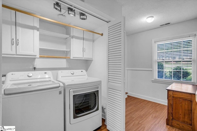 clothes washing area featuring cabinet space, visible vents, wood finished floors, baseboards, and washing machine and dryer