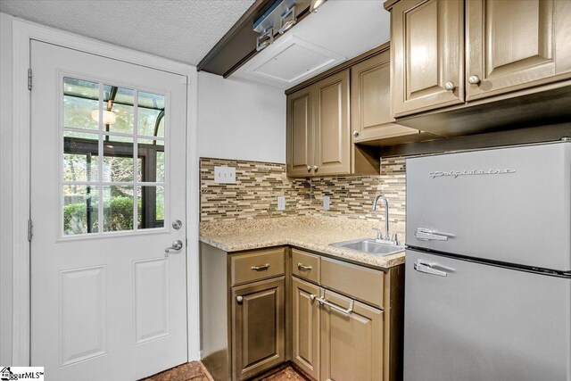 kitchen featuring tasteful backsplash, a sink, light countertops, freestanding refrigerator, and a textured ceiling