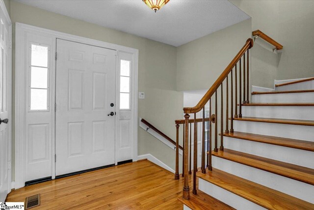 entryway featuring light wood-type flooring, baseboards, visible vents, and stairs