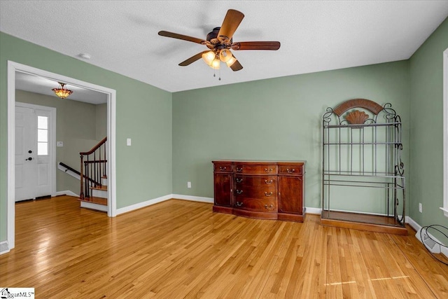 unfurnished living room featuring baseboards, a ceiling fan, light wood-style floors, and stairs