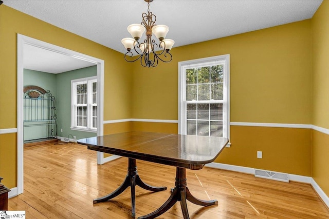 unfurnished dining area featuring baseboards, light wood-style floors, a notable chandelier, and visible vents
