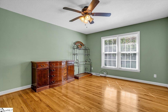 interior space with a textured ceiling, baseboards, a ceiling fan, and wood finished floors