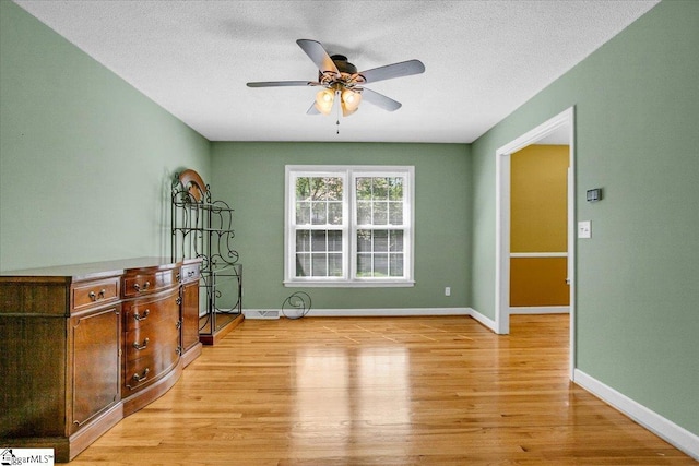 spare room featuring ceiling fan, light wood-type flooring, baseboards, and a textured ceiling