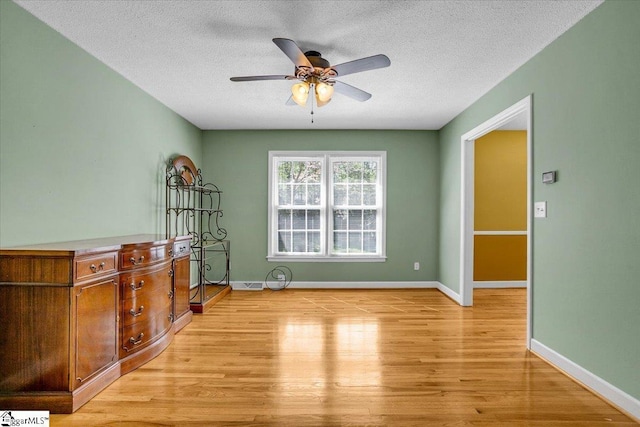 spare room with light wood-style floors, baseboards, a ceiling fan, and a textured ceiling