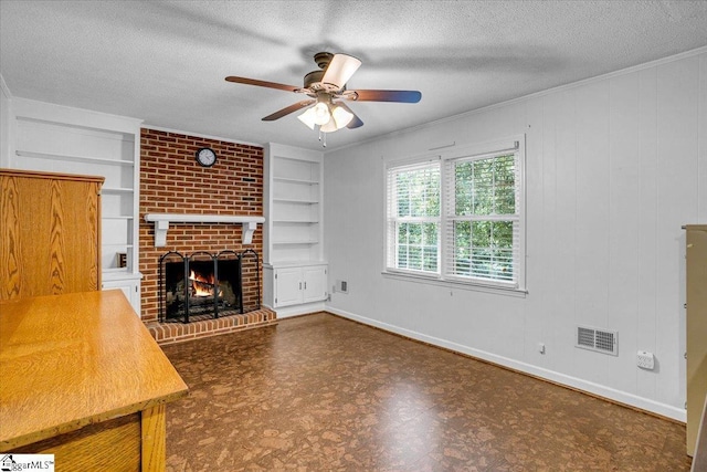unfurnished living room with built in features, ceiling fan, a textured ceiling, visible vents, and a brick fireplace
