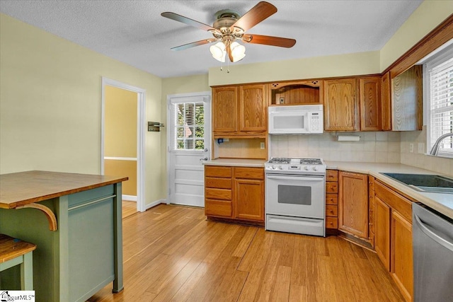 kitchen featuring light wood-style floors, ceiling fan, white appliances, tasteful backsplash, and a sink