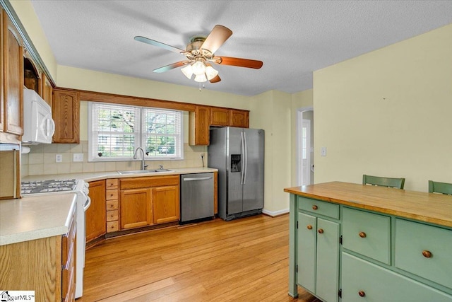 kitchen featuring light wood-style flooring, tasteful backsplash, appliances with stainless steel finishes, light countertops, and a sink