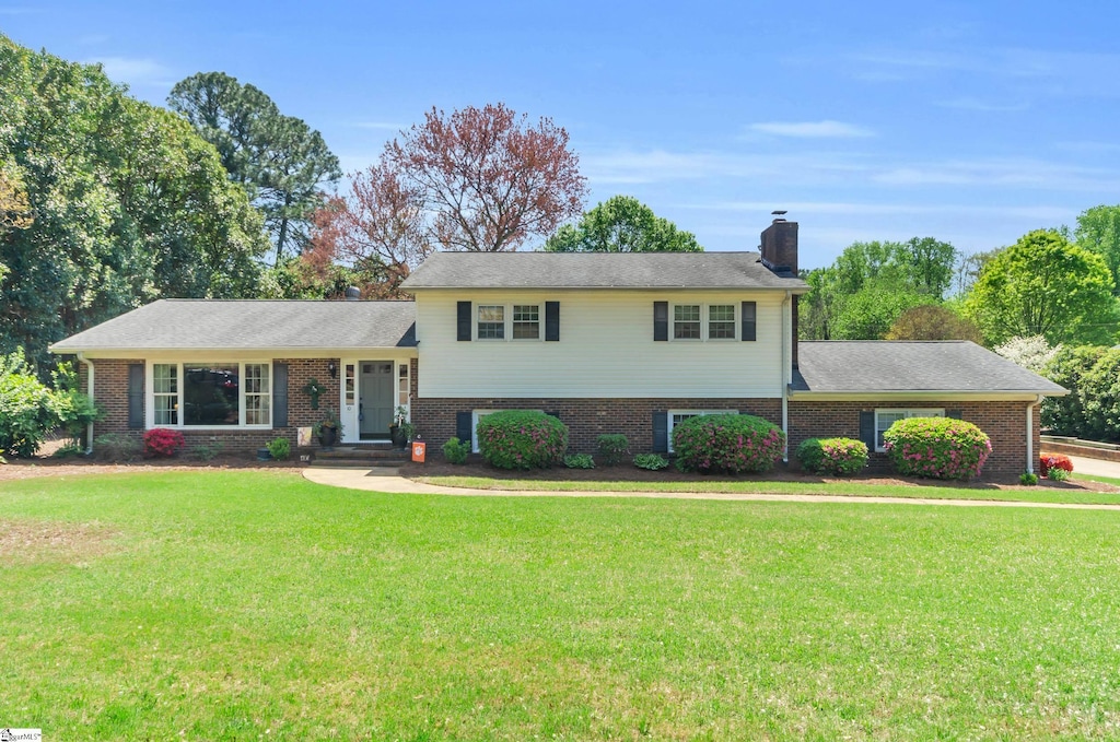 split level home with a chimney, a front yard, and brick siding