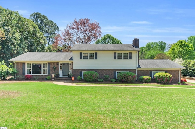 split level home with a chimney, a front yard, and brick siding