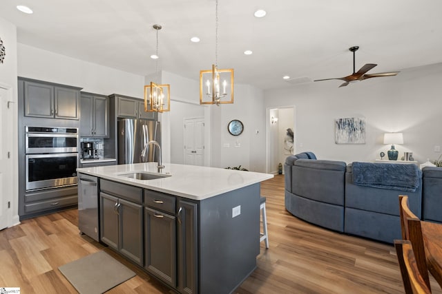 kitchen with a sink, open floor plan, light wood-type flooring, appliances with stainless steel finishes, and a center island with sink
