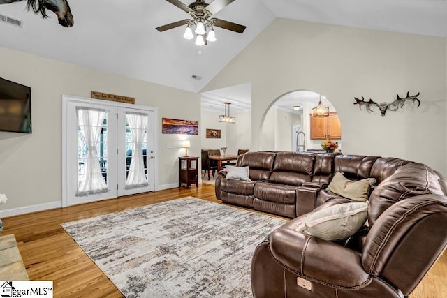 living area with light wood-style floors, high vaulted ceiling, arched walkways, a ceiling fan, and visible vents