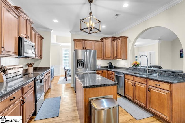 kitchen featuring a center island, arched walkways, a sink, light wood-type flooring, and appliances with stainless steel finishes