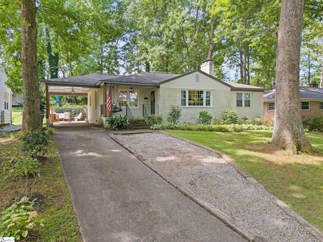 single story home featuring aphalt driveway, a porch, a front lawn, a chimney, and an attached carport