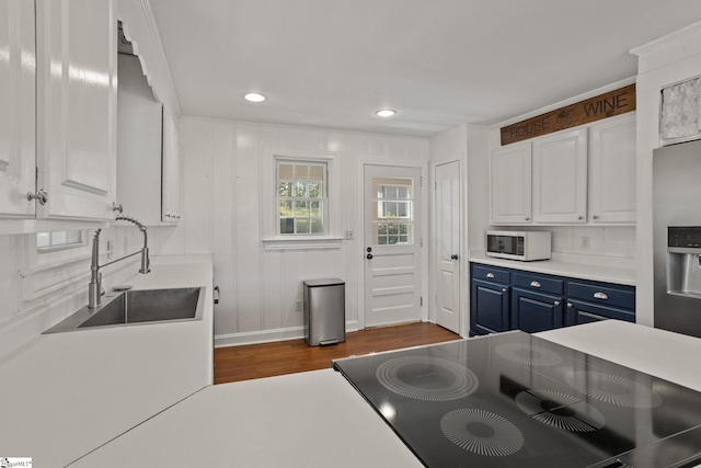 kitchen featuring a sink, dark wood-style floors, white microwave, stovetop, and blue cabinetry