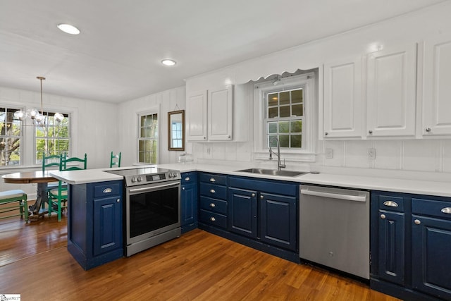 kitchen with stainless steel appliances, a peninsula, a sink, and blue cabinetry