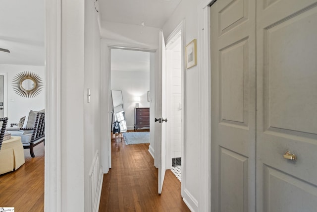 hall with visible vents, baseboards, attic access, and wood finished floors