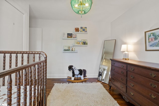 bedroom with dark wood-style flooring, baseboards, a crib, and a notable chandelier