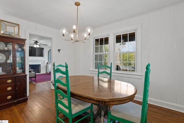 dining room with a decorative wall, a fireplace, ceiling fan with notable chandelier, and dark wood finished floors