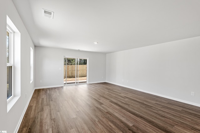 unfurnished room with dark wood-style flooring, visible vents, and baseboards