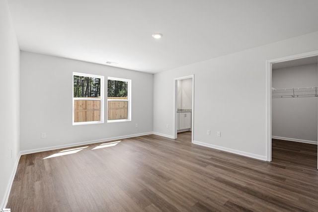 unfurnished bedroom featuring a spacious closet, dark wood-type flooring, visible vents, and baseboards
