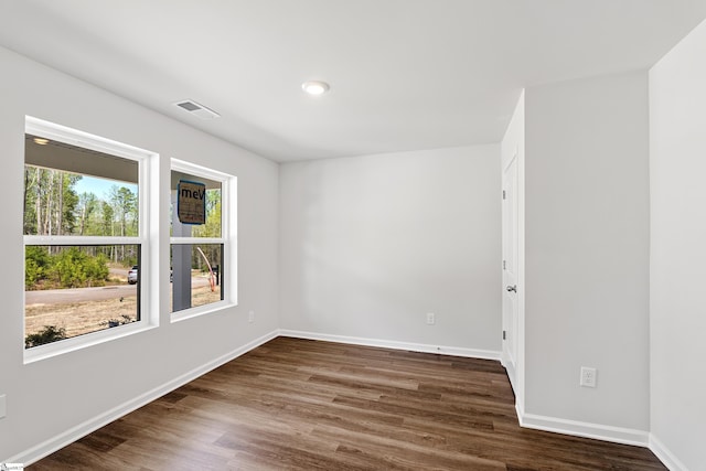 unfurnished room featuring visible vents, baseboards, and dark wood finished floors