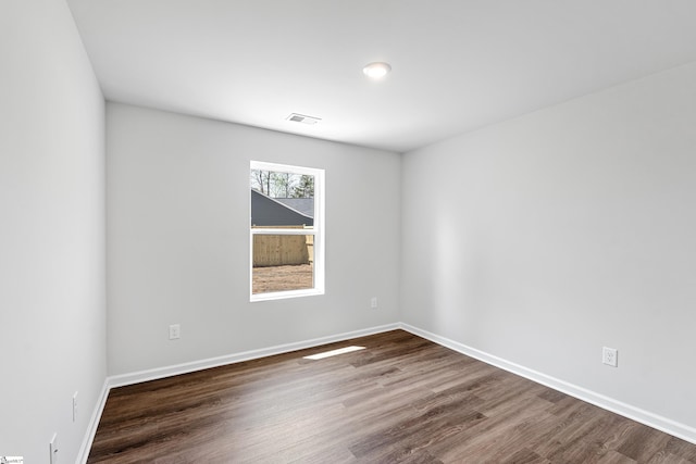 empty room with dark wood-style flooring, baseboards, and visible vents