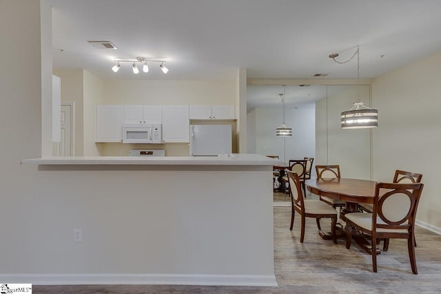 kitchen with white appliances, a peninsula, white cabinetry, light countertops, and visible vents