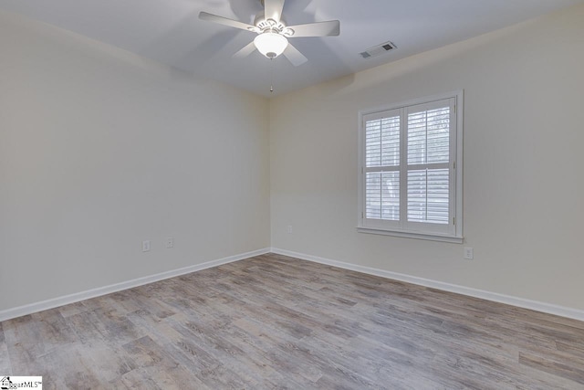 spare room featuring wood finished floors, ceiling fan, baseboards, and visible vents
