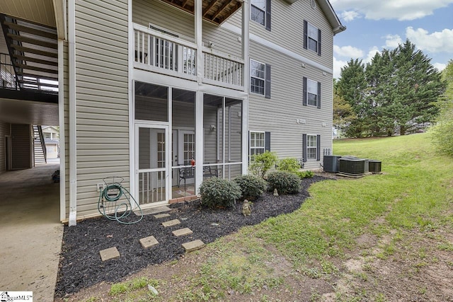back of property featuring a carport, central air condition unit, a balcony, a yard, and a sunroom