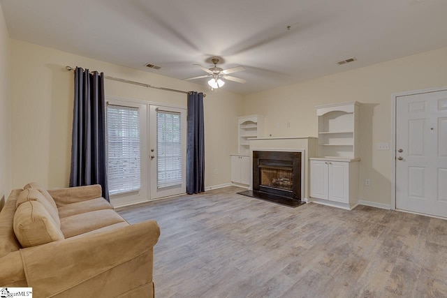 living room featuring light wood-style floors, a fireplace with raised hearth, visible vents, and a ceiling fan